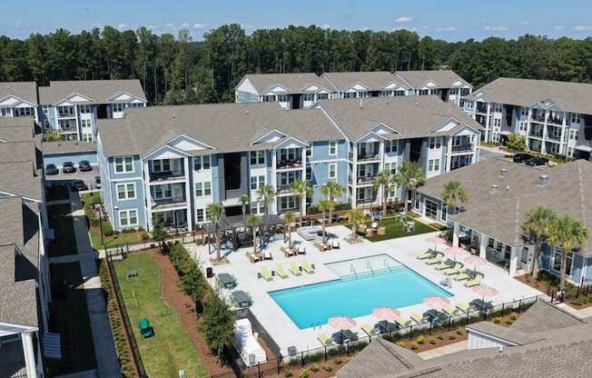 A large swimming pool surrounded by lounge chairs and umbrellas is the centerpiece of a resort-style apartment complex.