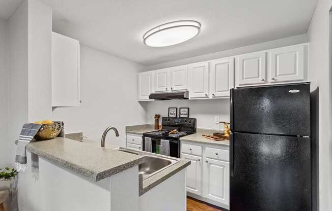 A black refrigerator is in the corner of a white kitchen.