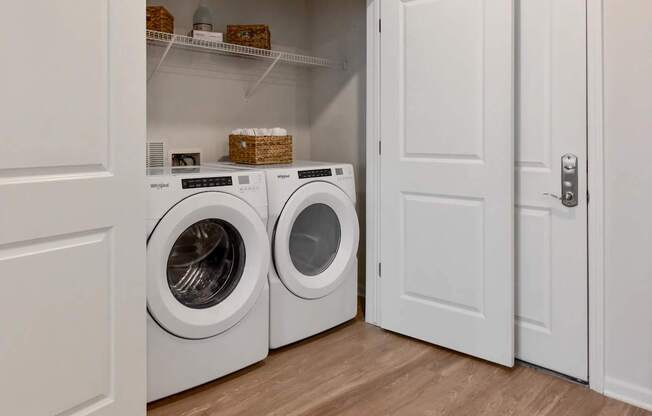 Two washing machines are in a white laundry room.