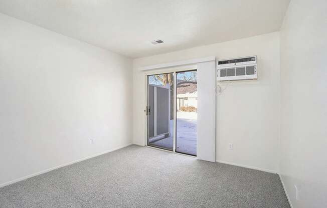 A room with a grey carpet and a white wall with a door leading outside.