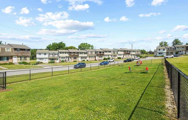 A grassy field with a fence and apartment buildings in the background.
