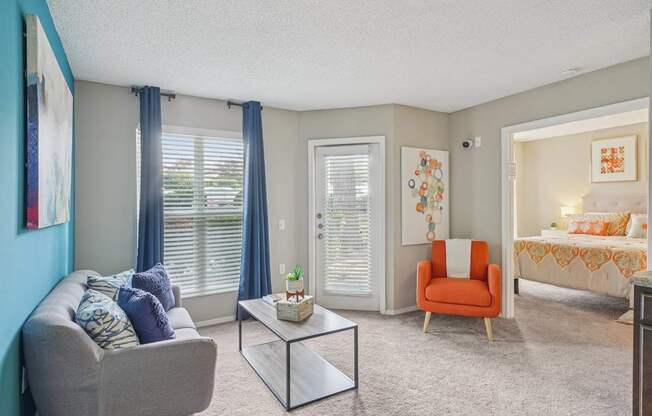 A living room with a grey couch, a glass table, and a red chair at The Falls Apartments in Raleigh NC