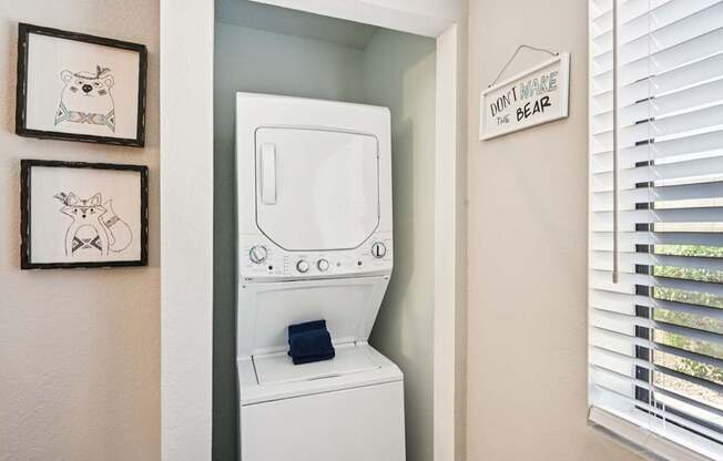 A white washing machine is in a small laundry room with a sign that says "Don't Make the Bear Sad" on the wall.