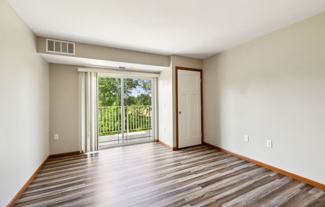 an empty living room with a sliding glass door to a balcony