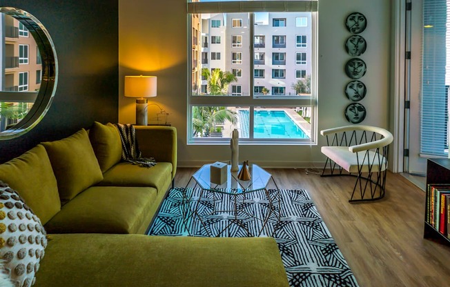 A living room with a yellow couch and a round mirror on the wall.