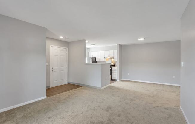 the living room and kitchen of an empty home with a carpeted floor