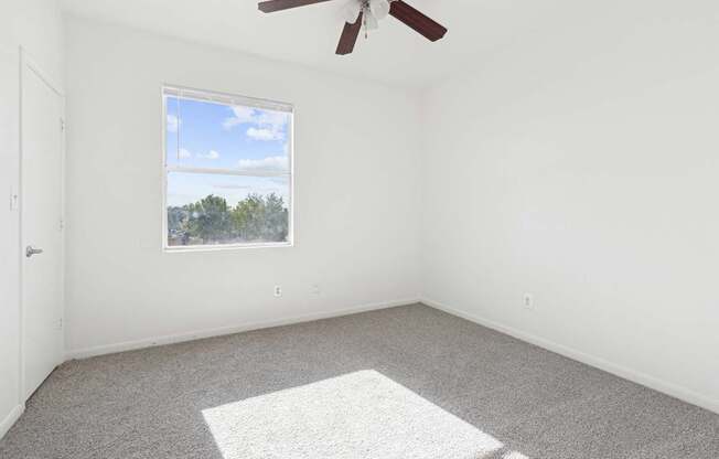 Affordable Apartments in Austin, TX for Rent- Huntington Meadows-  A room with a ceiling fan and a window overlooking a landscape.