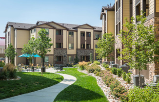 a sidewalk leading to an apartment building with lush green grass and trees