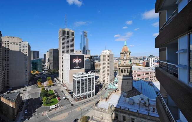 A cityscape with a mix of modern and older buildings, a clear blue sky, and a road with moving vehicles.