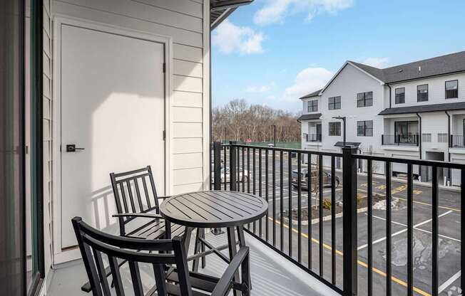 A balcony with a table and chairs overlooks a parking lot.