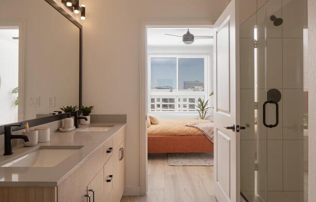 Dual sinks, matte black fixtures, and a glass-enclosed shower create a clean, connected bath that flows seamlessly into the bedroom.