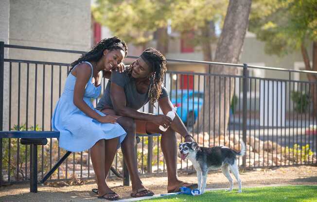 A man and woman sitting on a bench with a dog on the ground.
