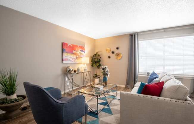 living room in Arlington Stadium 700 Apartments with glass table, blue chair, and large window with drapes.