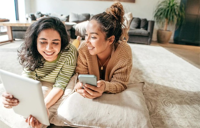 two women laying on the floor looking at a tablet computer