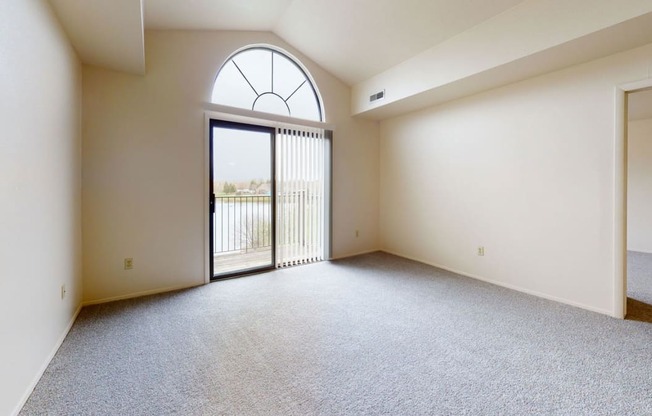 an empty living room with a cathedral ceiling and a glass door to a balcony