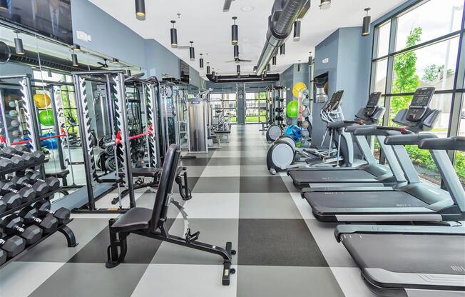 Large gym with hard checkered floor, ceiling fans, and rows of weight and cardio equipment