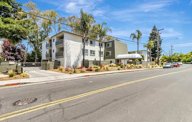 A street view of a residential area with apartment buildings and cars parked on the side of the road.
