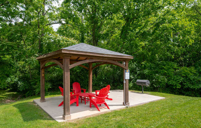 A wooden gazebo at The Retreat at Indian Lake Apartments in Hendersonville TN with red chairs is surrounded by greenery.