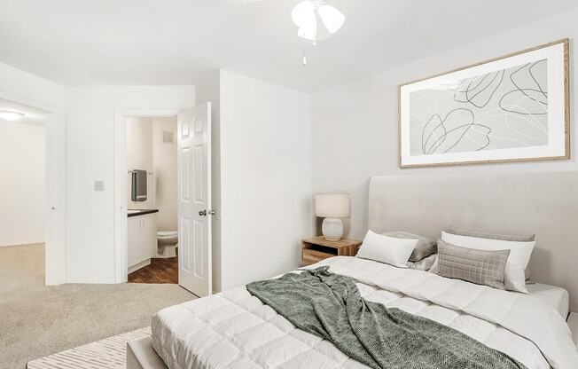 Virtually staged bedroom with carpet, accent rug, ceiling fan with light, wood side table looking into bathroom with wood flooring