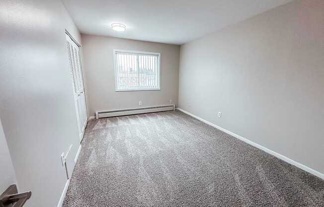 A room with a carpeted floor and a window with blinds.
