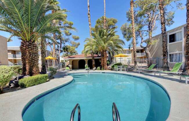 A swimming pool surrounded by palm trees and a building in the background.