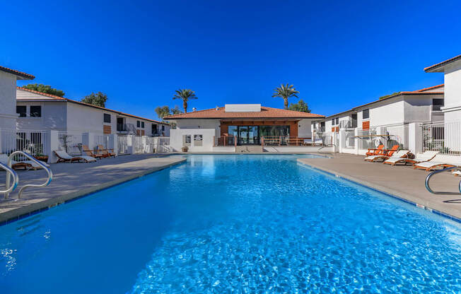 a swimming pool with lounge chairs and a building with a red roof in the background