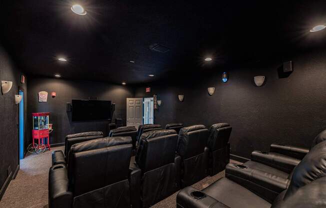 A dark room with a row of black leather chairs and a television mounted on the wall.