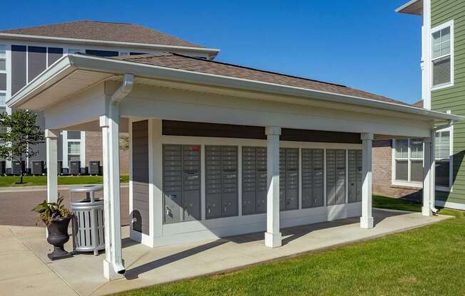 A small white building with a porch and a trash can in front of it.