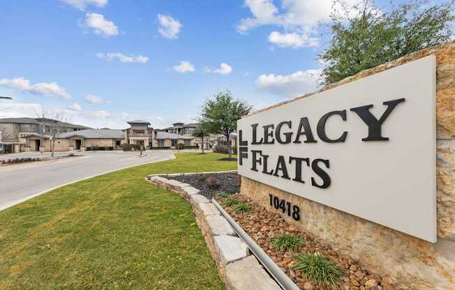 A sign that says Legacy Flats stands in front of a grassy area.