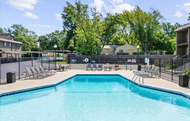 A large swimming pool surrounded by a fence and lounge chairs.