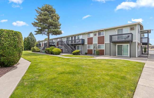 Apartment complex with a green lawn and a tree in the front at Wildflower Apartments in Kennewick, WA..