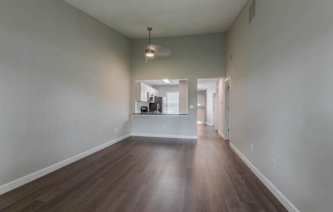 an empty living room with hardwood flooring and a hallway to a kitchen