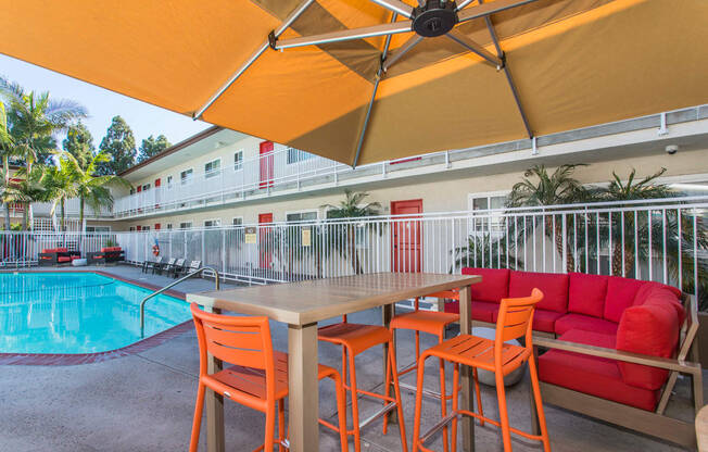 Outdoor Lounge area with table, bar stools and couch. Swimming Pool is several feet away from the lounge at Pacific Sands, San Diego, 92117