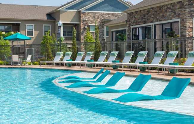 A row of blue lounge chairs are set up by a pool.