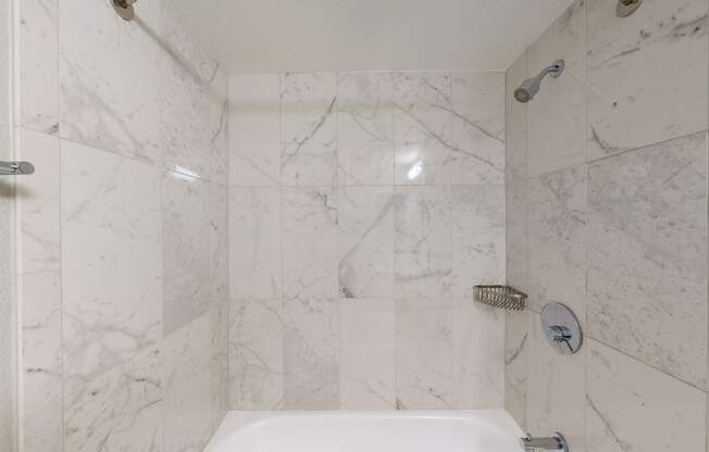 a bathroom with white marble walls and a white bathtub
