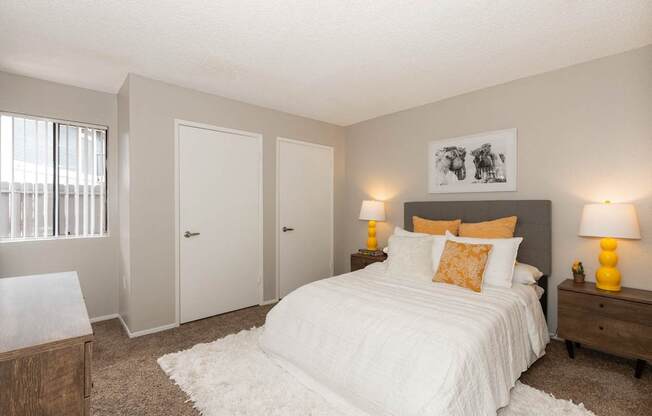 A bedroom with a large bed, two nightstands with lamps, and a window with blinds.
