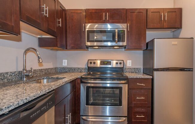 Studio apartment kitchen with steel appliances and brown cabinets