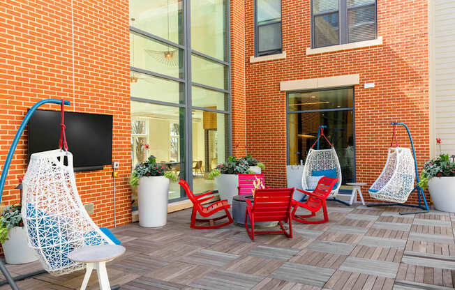 A red chair is on a patio with a blue chair and a white chair.