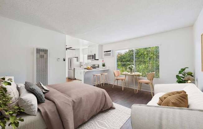 A bedroom with a bed, couch, and a dining area in the background.