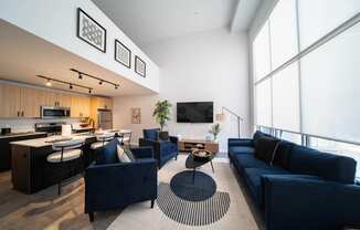 a living room with blue couches and chairs and a kitchen with a large window