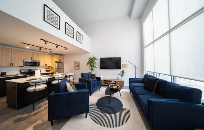 a living room with blue couches and chairs and a kitchen with a large window