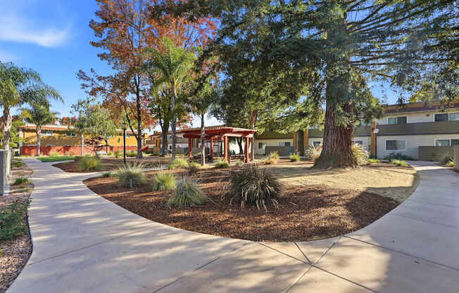 A tree-lined walkway leads to a building with a red roof.