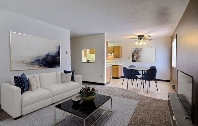 a living room with a couch and a coffee table in front of a dining room. Fargo, ND Prairiewood Meadows Apartments