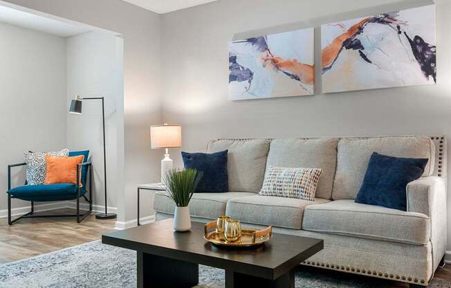 A living room with a grey couch, a blue chair, a black table, and two paintings on the wall.