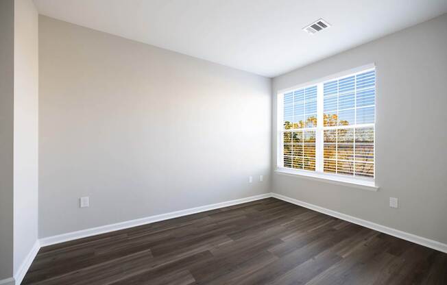 A room with wooden flooring and a window with blinds.