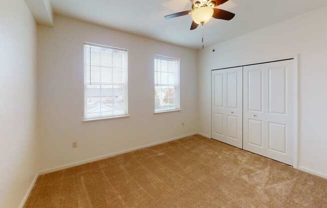 an empty bedroom with a ceiling fan and two windows