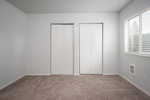 an empty room with two white closet doors and a window