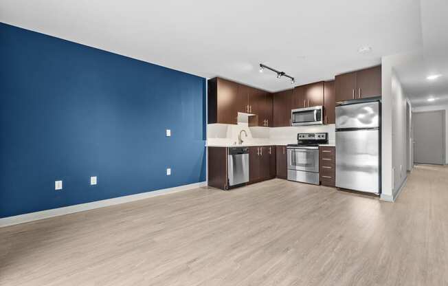 an empty room with a blue wall and a kitchen with stainless steel appliances