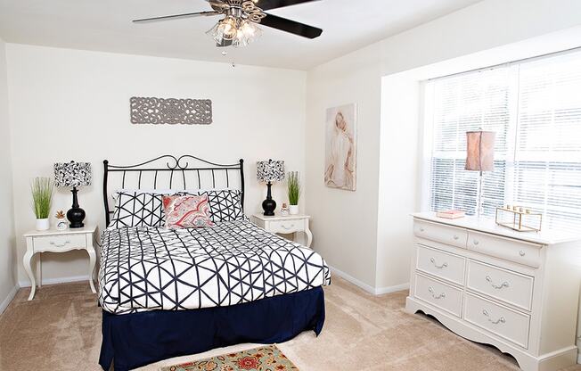 a bedroom with white walls and a black and white bedspread and a white dresser with