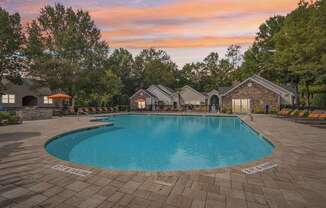 A large swimming pool surrounded by a brick patio and lounge chairs.
